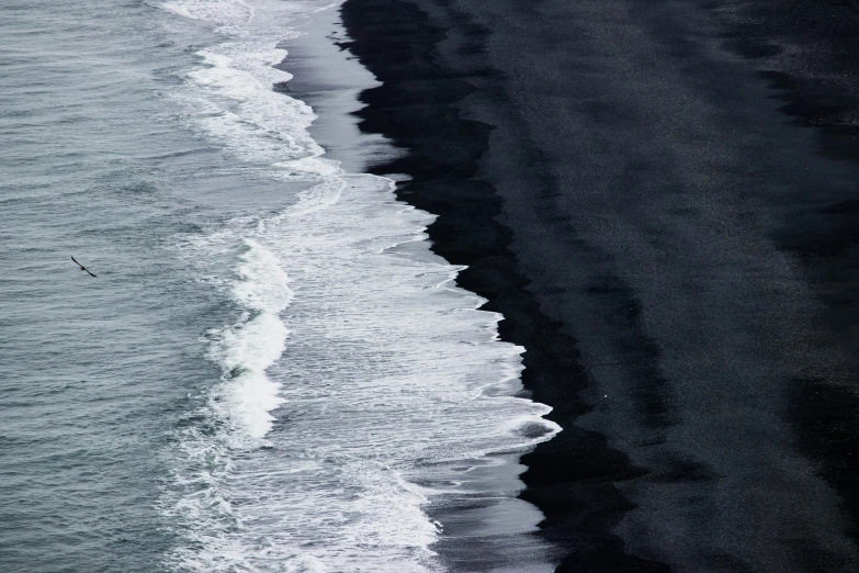 a black beach and the ocean with white foam