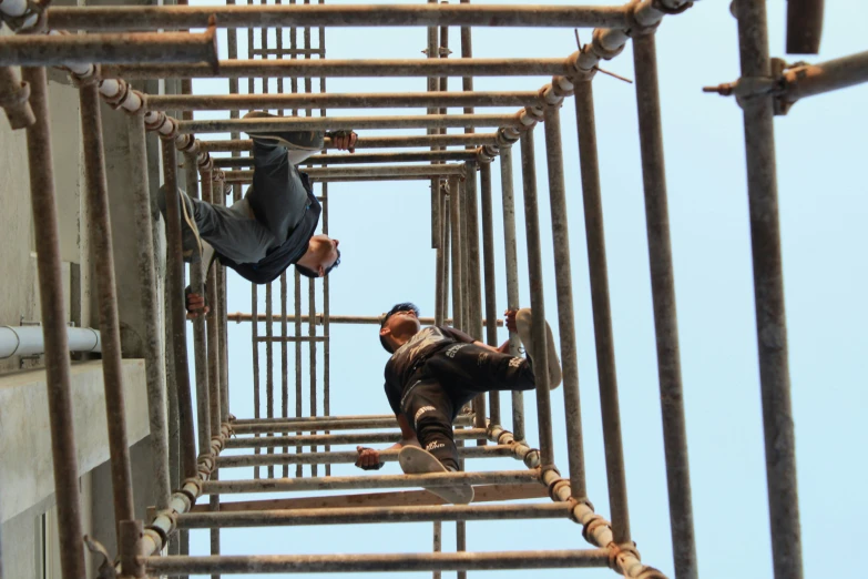 a man hanging from a ladder while another man rides