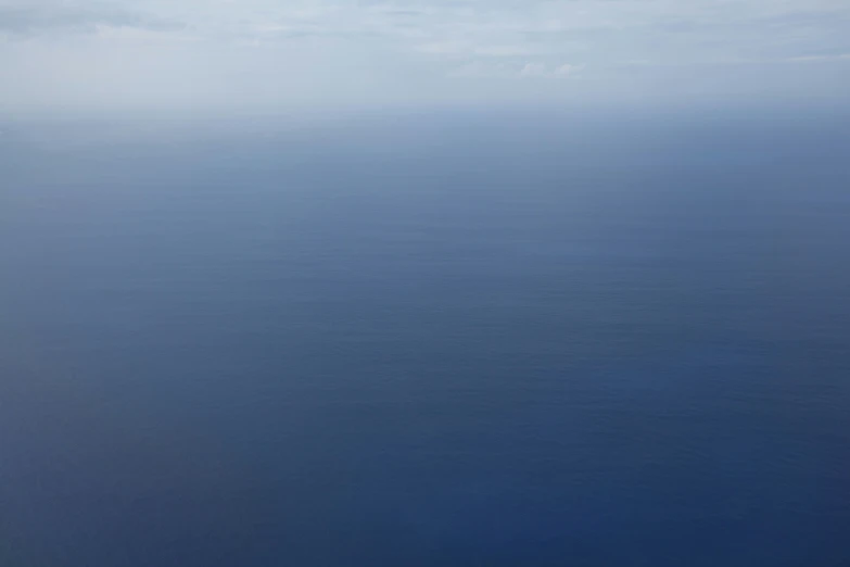 airplane flying over the water with clouds in the distance