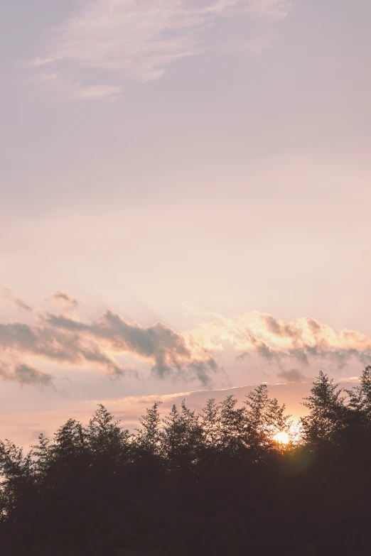 the sun is setting over some treetops and clouds