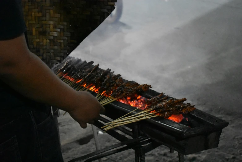 a person cooking dogs on top of skewers