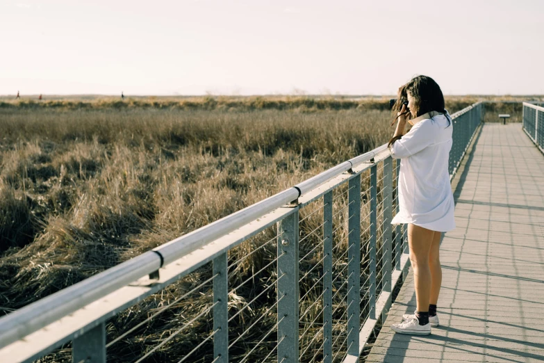 the woman walks along the boardwalk in the tall grass