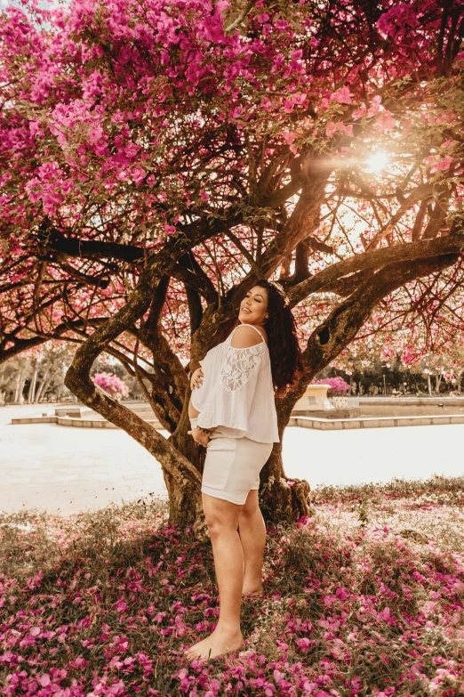 a beautiful young woman standing underneath a pink tree