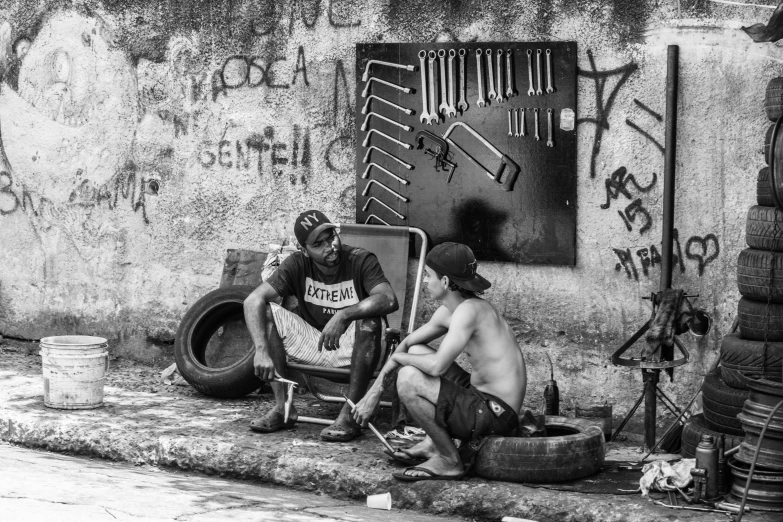 a pair of men sitting on a wall by some tires