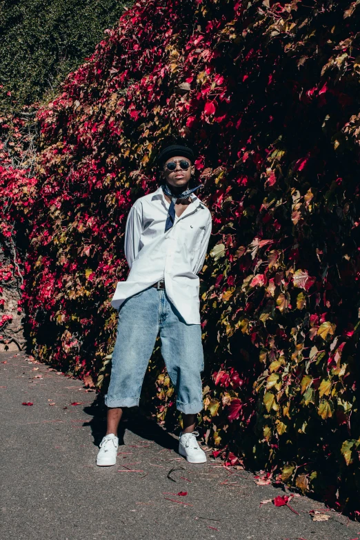 a man in blue jeans and tie standing by some flowers