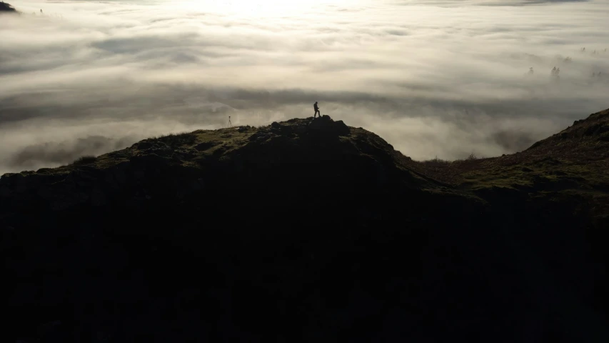 a man standing on top of a mountain under some clouds