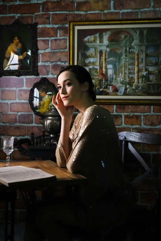 a woman sitting at a wooden table in front of a wall with paintings on it