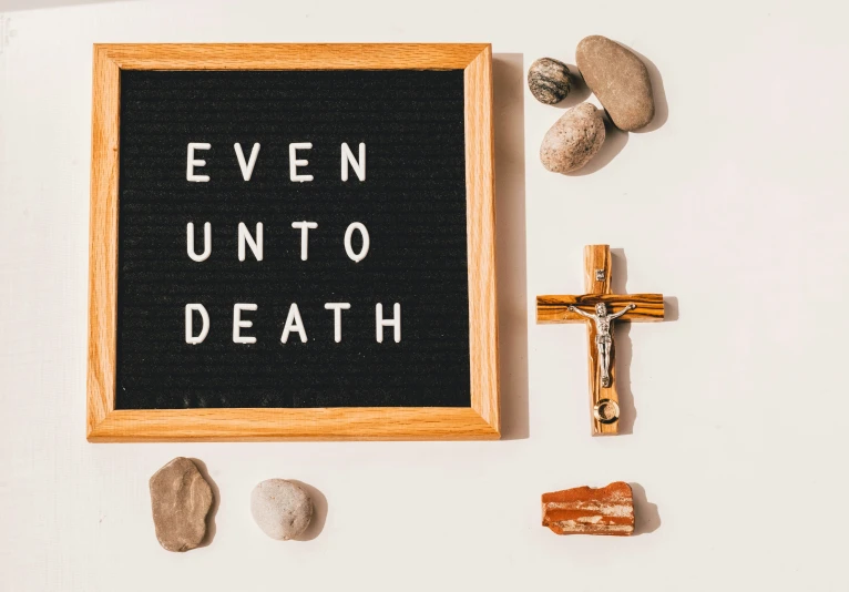 a blackboard with the words even unto to death next to rocks and a cross