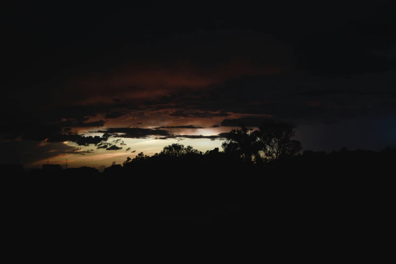 the sky with clouds and trees silhouetted in bright moonlight