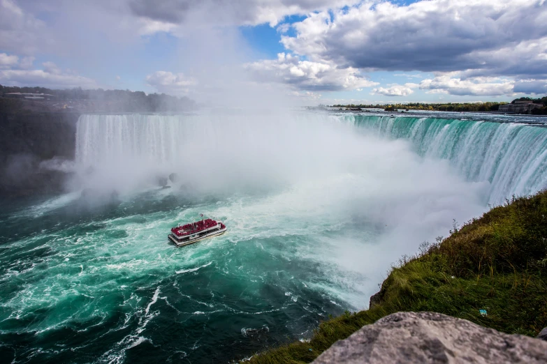 a small boat in the water with an incredible waterfall in the background