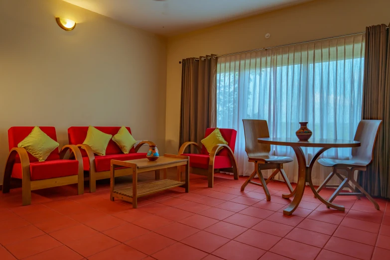 a red couch, three chairs and table with green pillows and curtains