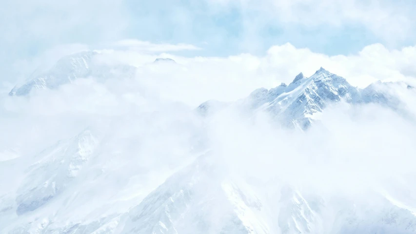 a very tall snow covered mountain peak under a cloudy blue sky