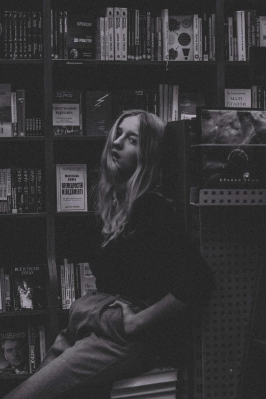 a lady sitting on a window sill in front of a book shelf