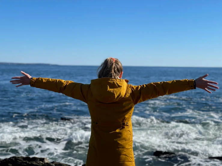 a woman looking out at the ocean and holding her arms out