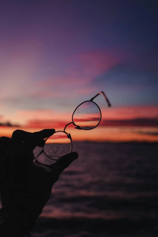 a person holding up two metal scissors at sunset