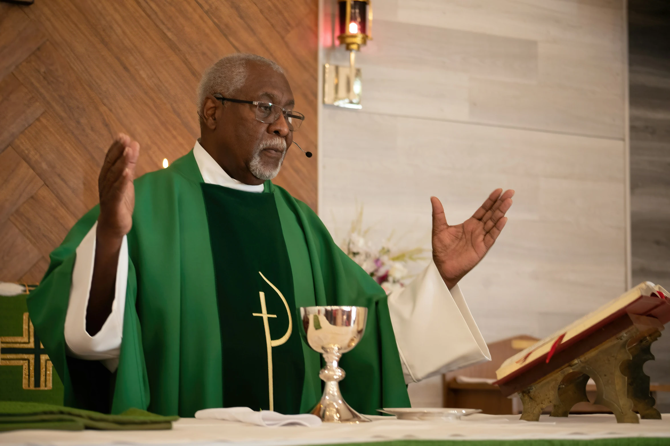 a priest sitting at his desk clapping while standing behind a microphone