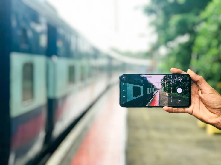 someone is holding up their cell phone while taking a picture of the back of a passenger train