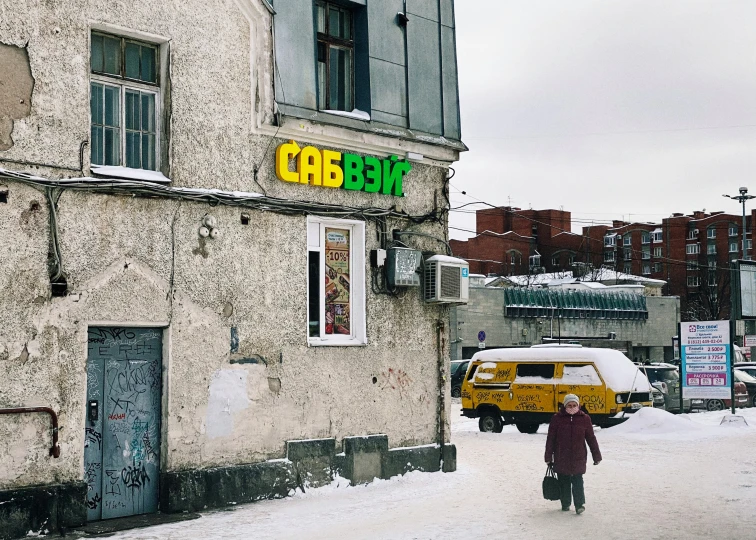 a woman walking down the sidewalk of a building in the snow