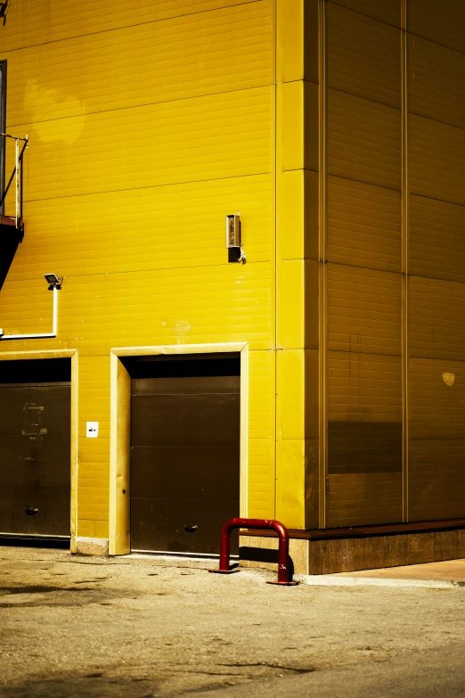 the yellow wall of an industrial building has two parking doors