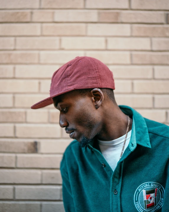 man in maroon hat standing against a brick wall