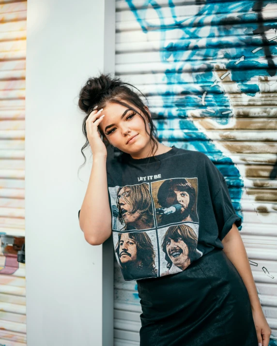 a woman leaning against a wall wearing a t - shirt with a beatles image