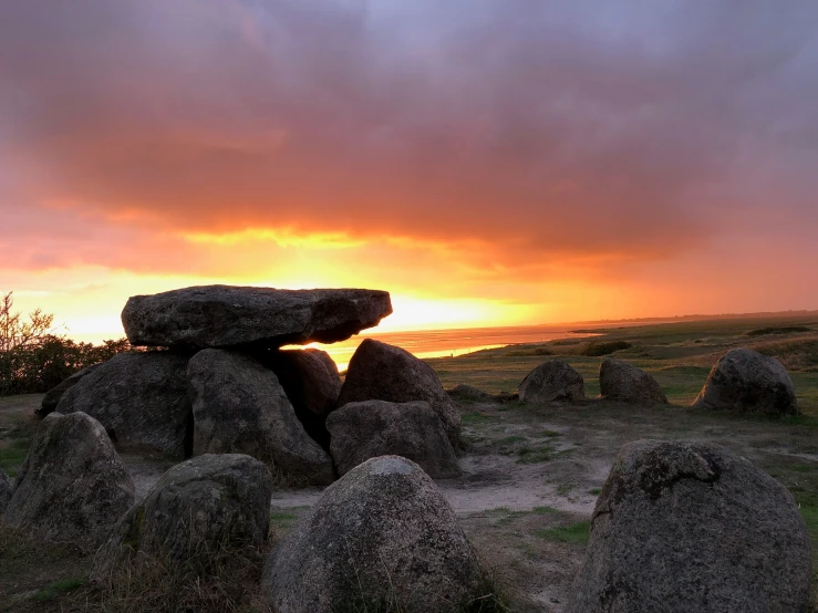 a field with large rocks and a sunset behind it