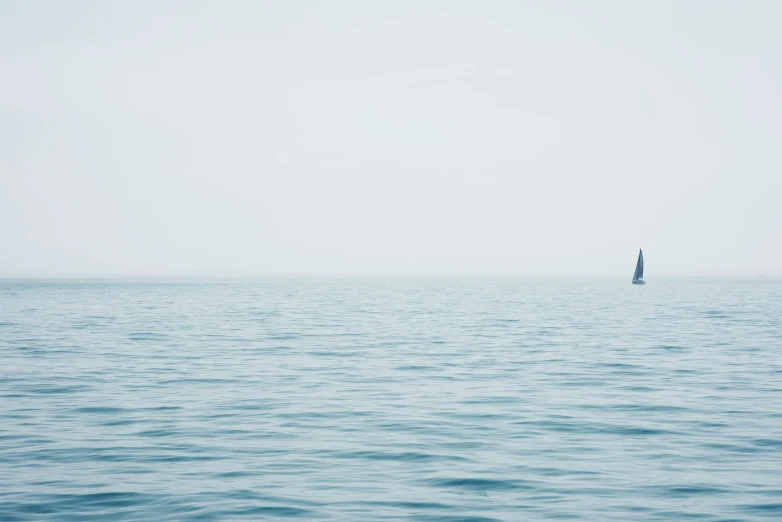 a small sailboat in the ocean near an oil rig