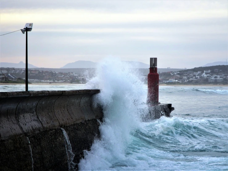 a rough ocean in the foreground with lighthouse at the end of the pier