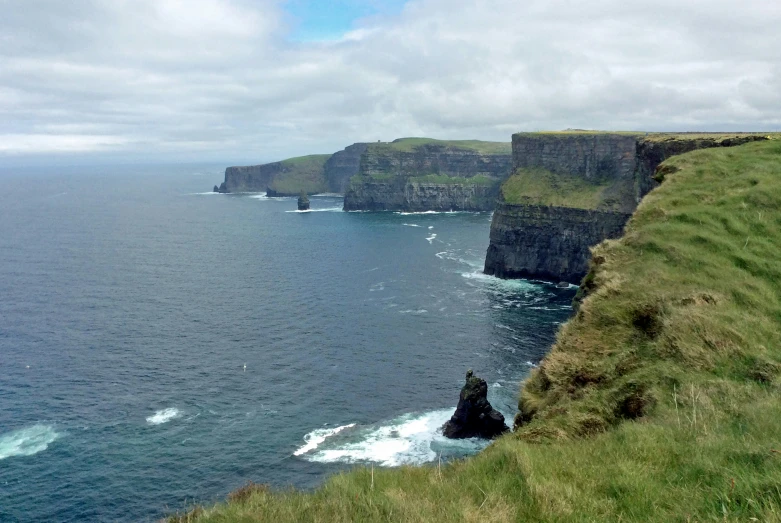 a cliff with many cliffs and green grass near the water