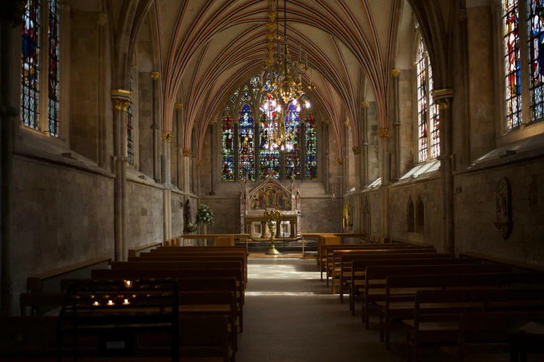 a dark church filled with wooden pews next to stained glass windows