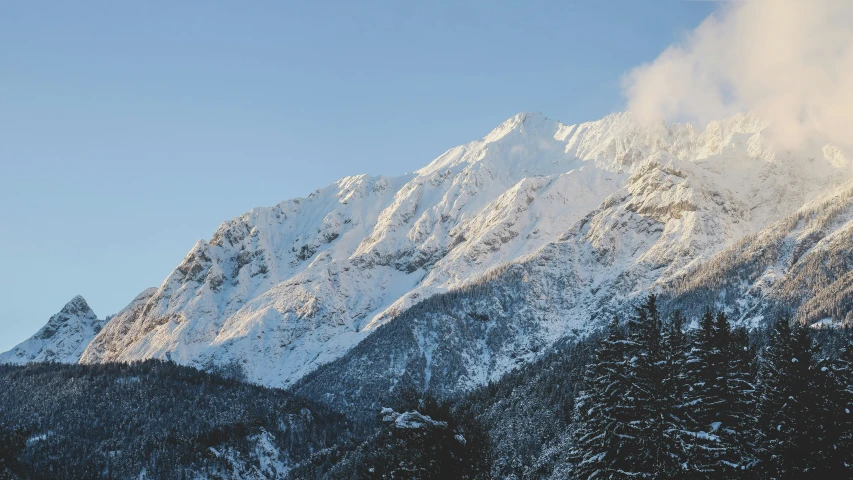 a snowy mountain with trees and clouds