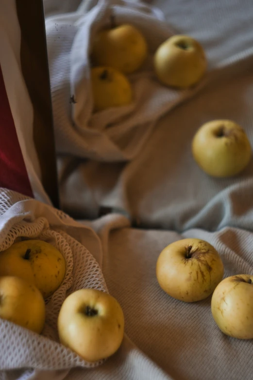 yellow apples laying on a white cloth on top of a bed