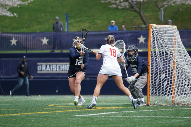 three female lacrosse players on a field playing a game