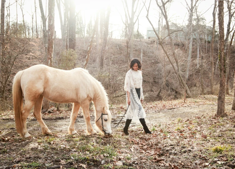 a woman standing with her back to the camera while feeding a horse