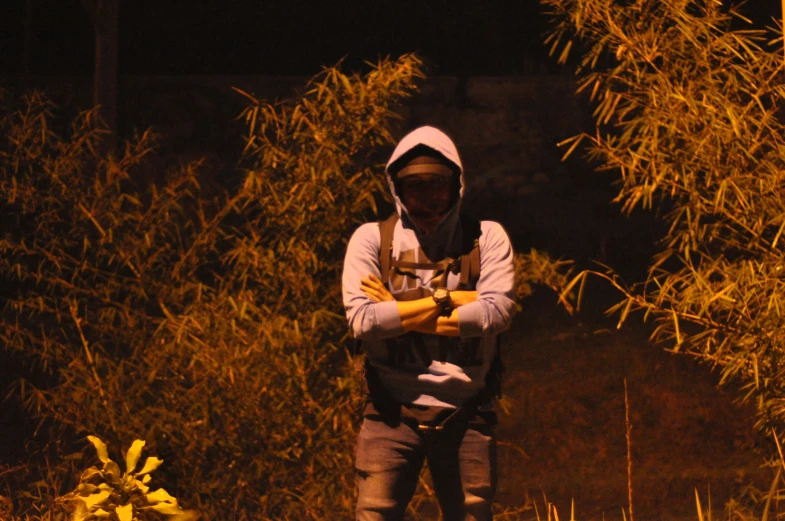 a man holding an apple while standing by a bush at night