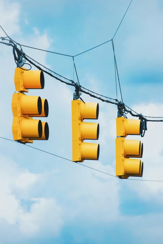 three yellow traffic lights hang from wires in the sky