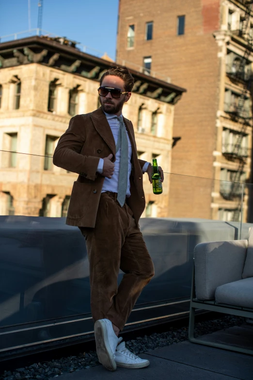 a man stands on a sidewalk with sunglasses on and holding a bottle