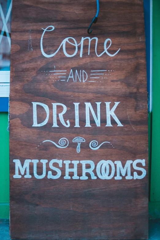 a brown sign that reads come and drink mushrooms