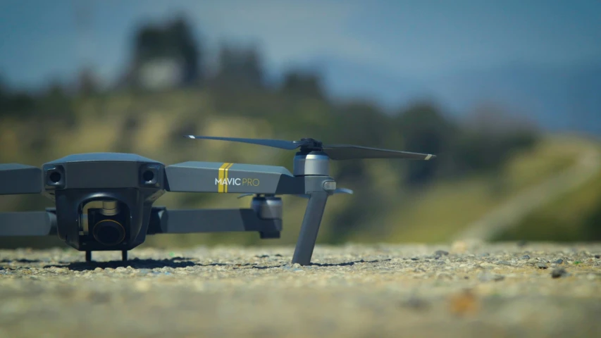 a small gray djrobott with yellow and white markings sits on a gravel surface