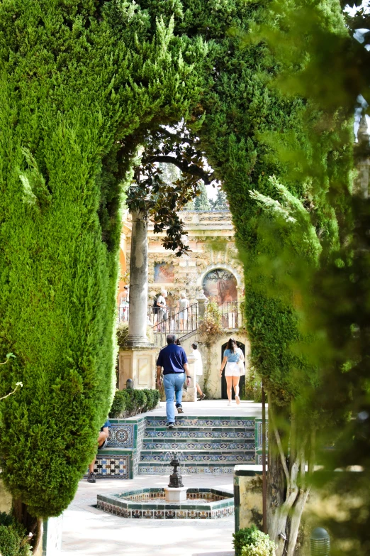 people are gathered around in the garden in front of a fountain