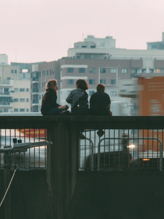 three people sitting on the railing looking over the city