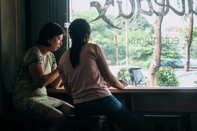 two women sitting at a window looking in to the street