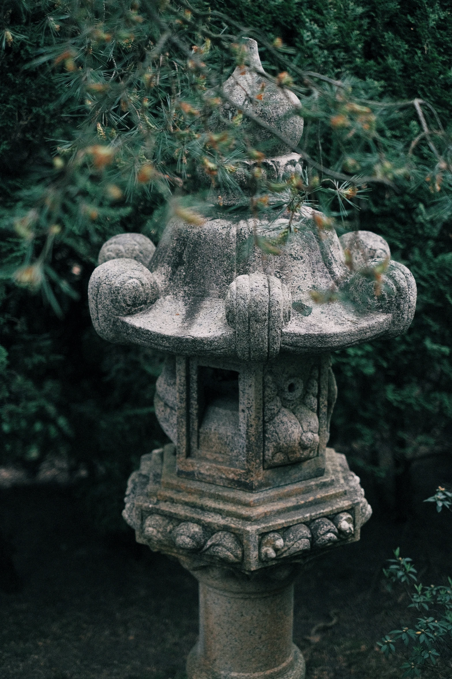 a small statue stands in the bushes near a shrub