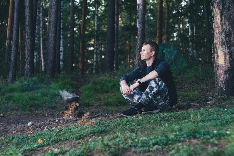 a man sitting next to a fire in the woods