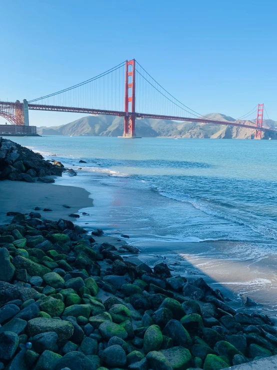 a large bridge crosses over the ocean near a rocky beach