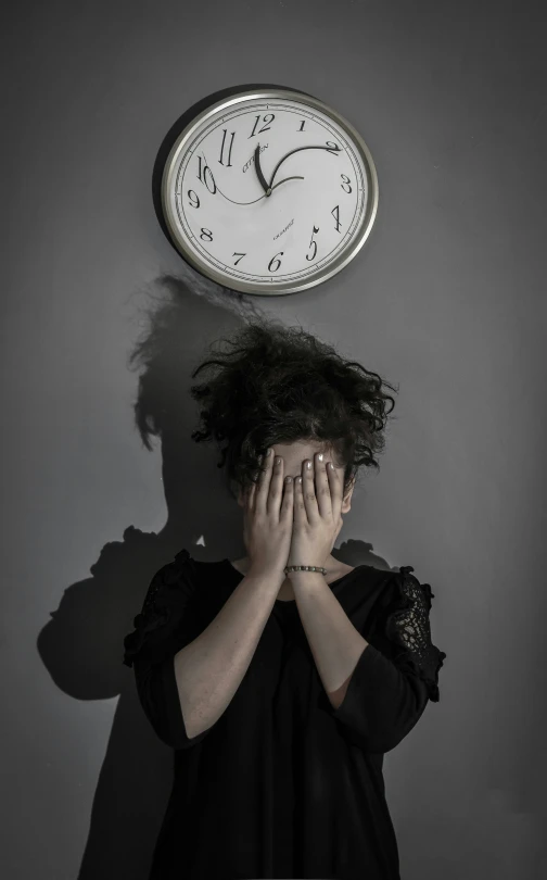 a person covering their eyes next to a wall clock