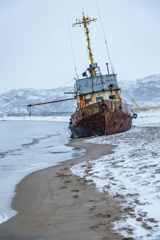 an old ship in the water in front of snow covered hills