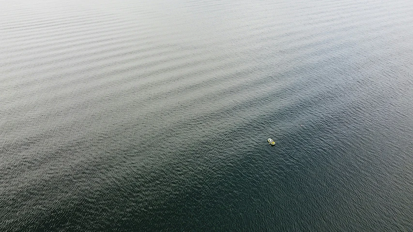 two small boats out in the distance, one white and one black, are seen from an over head view of the water