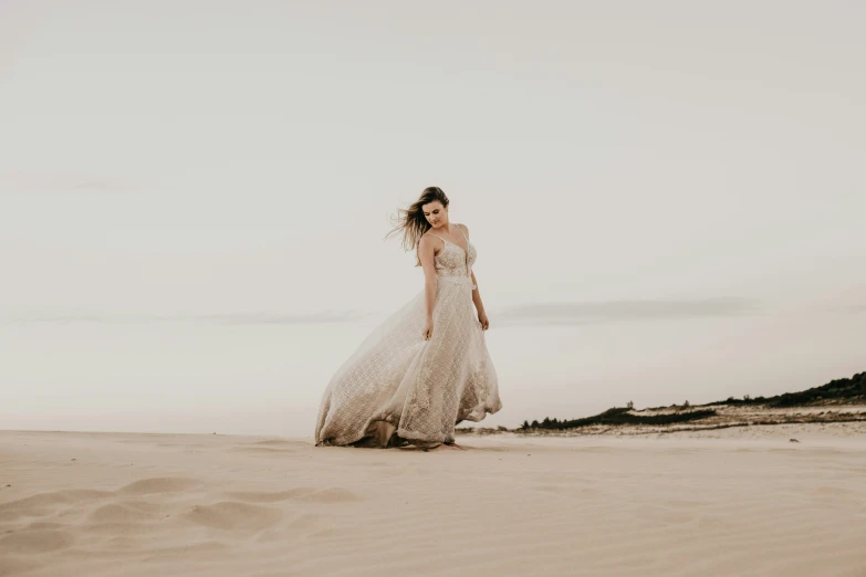 the woman in the wedding dress is standing in the sand