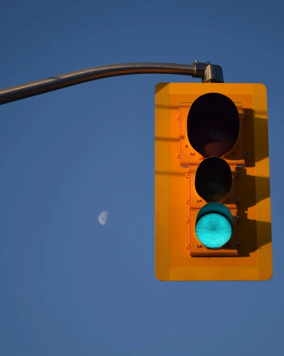 a closeup of an yellow traffic light with a crescent on a blue sky background